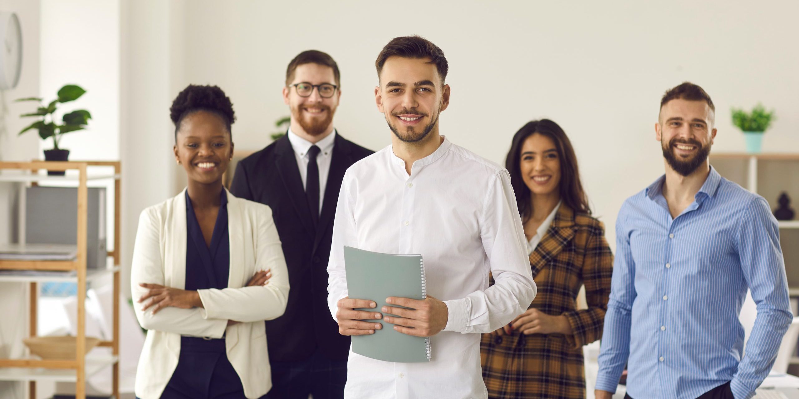 Portrait of confident successful young business male leader with diverse interracial smart people team looking at camera smiling standing in modern office. Leadership, cooperation, teamwork concept